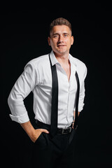 A stylish young man in a white shirt with rolled-up sleeves poses on a black background. A handsome charismatic businessman.