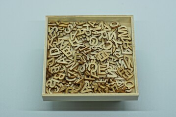 pile of small brown gray wooden letters lie in a square box on a white table