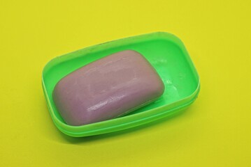 one purple bar of soap lies in an open green plastic soap dish on a yellow table