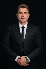 A handsome young man in a stylish black suit poses on a black background. A stylish business man. A big businessman.