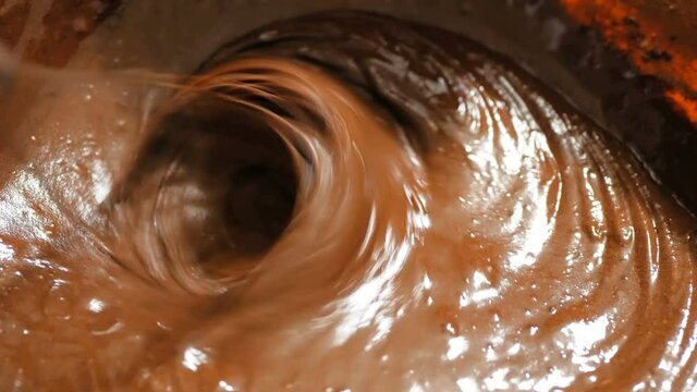 The chef mixes the chocolate cream for the cake with a mixer. Close-up of a chef stirring a chocolate dough with a blender to make a brownie.