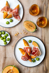 Fototapeta na wymiar Fresh cantaloupe melon with jamon or prosciutto and green olives with glass of wine. Traditional Spanish and Italian appetizer, antipasti snack. Top view