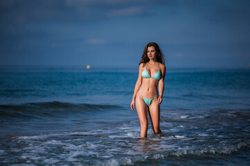 Fototapeta na wymiar Fitness model girl posing in the sea in green color mini bikini.