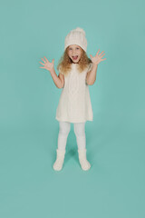 beautiful happy little blue-eyed blonde girl in a knitted winter hat and a knitted white dress