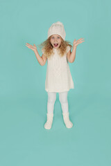 beautiful happy little blue-eyed blonde girl in a knitted winter hat and a knitted white dress
