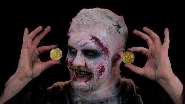 Creepy man with bloody scars face, Halloween zombie showing golden bitcoins. Achievement career wealth, cryptocurrency investment, mining, future technology. Scary wounded undead guy smiles terribly