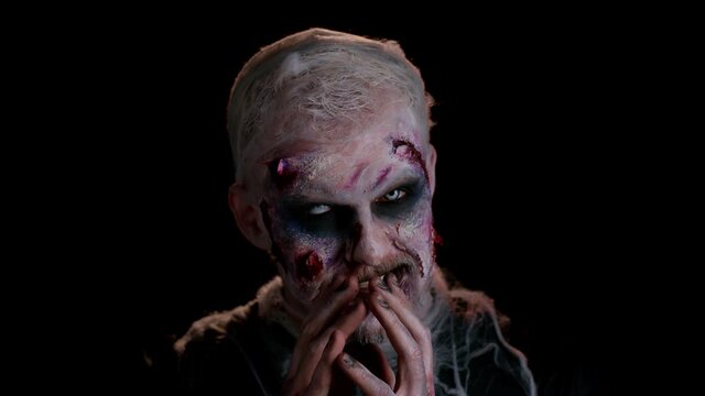Creepy man with bloody scars face, Halloween stylish zombie make-up. Scary wounded undead guy making faces, looks at camera and smiles terribly in police lights. Thematic party. Sinister beast monster