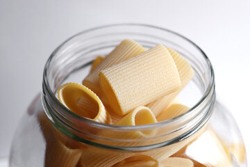 Glass jar filled with dry paccheli yellow pasta over isolated white background. Rigatoni pasta in a glass apothecary jar.