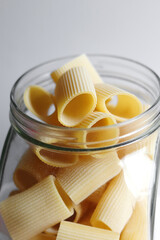 Glass jar filled with dry paccheli yellow pasta over isolated white background. Rigatoni pasta in a glass apothecary jar.