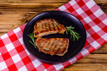 Plate with roasted steaks and rosemary twigs on a wooden table