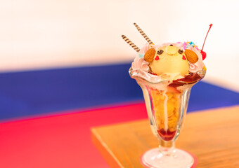 Japanese dessert of an artist ice cream depicting a cute bear character face in a stemware glass made topped with pink sweet whipped cream, corn flakes, almonds and cherry fruit.