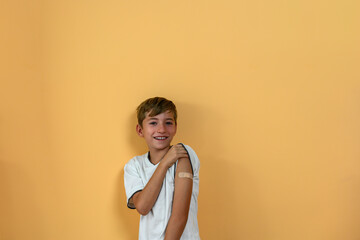 Smiling teenage boy shows a band aid on his arm. Vaccine concept