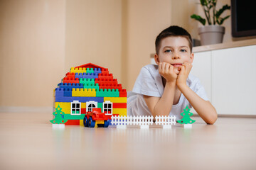 A little boy plays with a construction kit and builds a big house for the whole family. Construction of a family home.