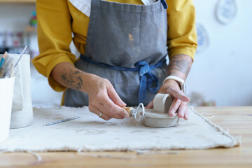 Hands of female artisan working with raw clay in pottery studio. Young student girl or master preparing material for shaping ceramic kitchenware and modeling jar. Pottery business and workshop concept