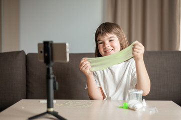 child girl 8 years old schoolgirl blogger making slime broadcasts via phone at home. High quality photo