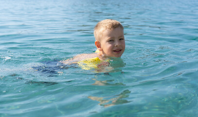 Fototapeta na wymiar The child learns to swim. Happy child swims in the sea. Holidays in Greece