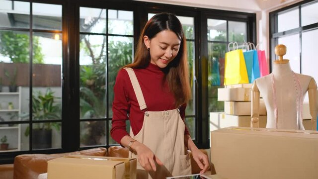 Young Asian woman receive phone call via mobile phone from customer then she check product in workplace room. Concept of small business with new modern lifestyle.