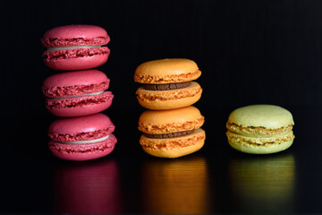 Stacked red orange and a green Macaron dessert cookies made from meringue and almond reflected on black table