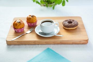 Breakfast presented on a wooden board with a cup of black coffee, muffins and a doughnut