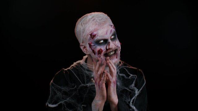 Sneaky cunning zombie man with makeup with wounds scars with tricky face gesticulating and scheming evil plan, thinking over devious villain idea, cunning cheats, jokes and pranks. Sinister dead guy