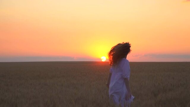 Beautiful caucasian woman is running in the field. The girl is dancing in nature. Mother nature. Have fun at sunset. The sun is golden on the horizon. Touch the wheat with your hands. Romantic dress.