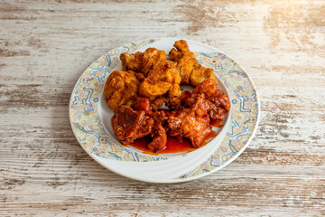 Breaded fried chicken pieces dipped in Korean spicy sauce on light wooden table