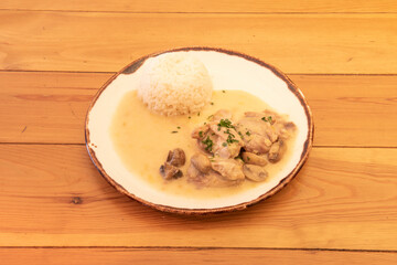 Chicken stroganoff recipe with mushrooms, chopped parsley and white rice garnish on wooden table