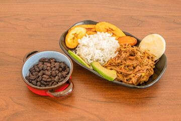 Venezuelan recipe for pabellon with black beans, ripe avocado, shredded pork, white rice, arepas and fried ripe plantain