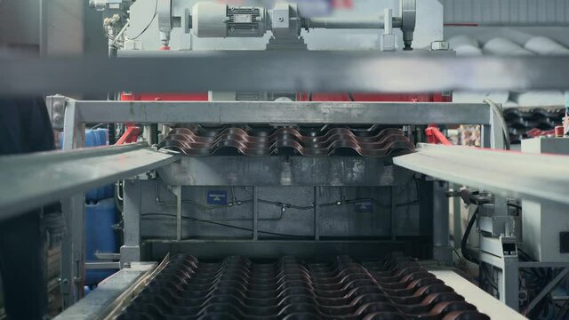 Metal sheet forming machine in factory for production materials for roof and facade of buildings. Production metalwork line in process of manufacturing metal tiles and siding.