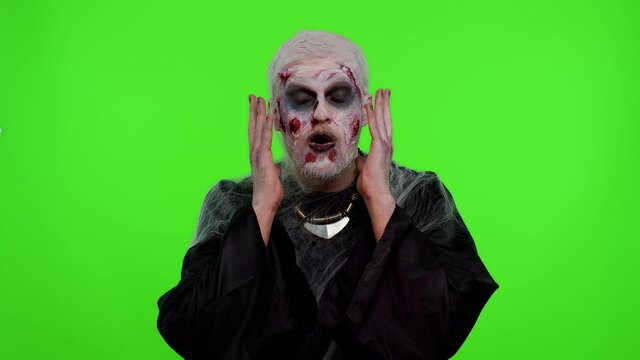 Oh my God, Wow. Frightening man with Halloween zombie bloody wounded makeup raising hands in surprise looking at camera with big eyes, shocked by sudden victory. Excited amazed sinister undead guy