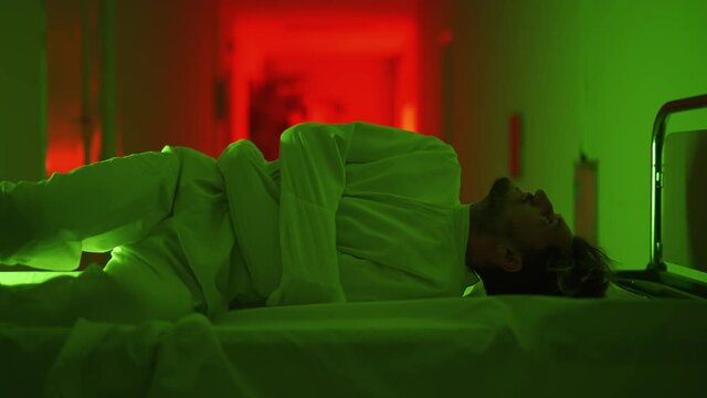 A mad male patient in straitjacket is lying on gurney and going crazy in a mental hospital. Mentally ill man with bipolar or psychic disorders. Concept of paranoia or schizophrenia and madness.