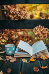 Naklejka na ściany i meble Book Pages Turning In The Autumn Wind, Close Up. Open book and cup of tea on an old deck covered with fallen yellow leaves. Cozy magical fall aesthetics. 