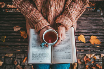 Woman Holding Steaming Cup of Tea or Coffee and Reading a Book, Enjoying Cozy Morning. SLOW MOTION, CLOSE UP. Unrecognizable Girl hands with a mug of hot drink indoors. Cinematic light. Lens Flare.