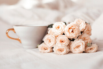 Obraz na płótnie Canvas Cup of tea and white roses on bed background. Romantic morning breakfast at bed.