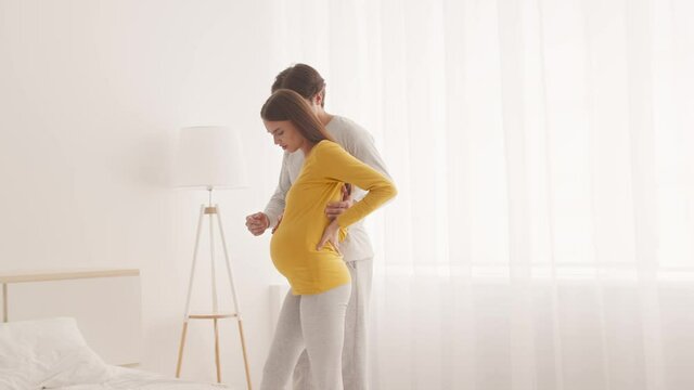 Health problems during pregnancy. Young pregnant woman suffering from backache, her loving husband leading her to bed