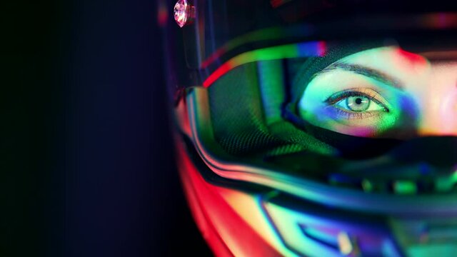 Half female attractive motorcyclist woman face in motorcycle helmet. Macro view of bikers eye with glowing neon colorful light. Trip, cafe racers, speed, freedom concept. Copy space.