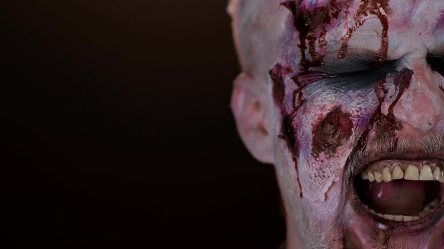 Close-up macro frightening man face with Halloween zombie blood flows and drips on face, trying to scare. Horror theme. Sinister undead guy isolated on studio black background. Serious injury wound