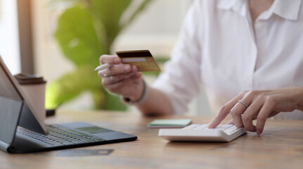 Fototapeta premium Woman making calculations and shopping online with credit card. Female using calculator, budget and loan paper in office. Bills, home budget, tax, savings, finances, economy, audit, debt concept