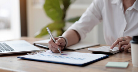 asian businesswoman or accountant working pointing graph discussion and analysis data charts and graphs and using a calculator to calculate numbers.Business finances and accounting concept