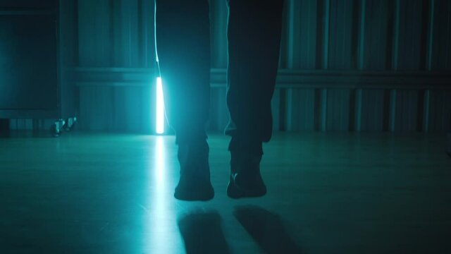 A young man skipping in bare feet in a gym room with blue lights around him. A person working out doing exercises in a dark and moody setting
