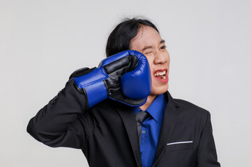Isolated studio shot of Asian crazy stress depress mad male businessman in black formal suit standing wears blue boxing glove punching and hurting own face shouting with pain on white background