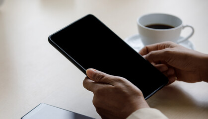 Close up shot of blank black screen touchscreen tablet computer holding in hands of unrecognizable unidentified businesswoman for advertising text and copy space near smartphone and hot coffee cup