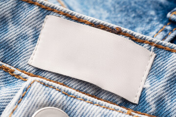 Blue jeans with a white blank label, close-up. Jeans texture. Fashion denim background for sewing, copy space. Label on clothing to indicate the size, company