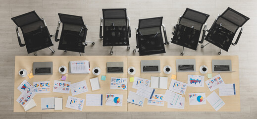 Table top view of wooden conference table with charts and graphs papers and laptop on it and six chairs lying in straight line beside the table in office. Concept for business meeting