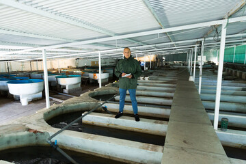 Man in working clothes controlling fish growth in trout hatchery incubator