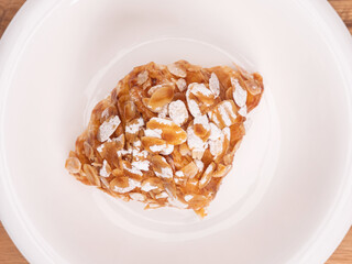 top angle of fresh croissant covered almond slide mixed sweet caramel and topping with sugar powder on a white plate placed on white table top.