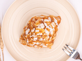 top angle of fresh croissant covered almond slide mixed sweet caramel and topping with sugar powder on a pastel plate placed on white table top.