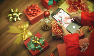 Fototapeta na wymiar Person on sweater using smartphone to take snapshot of luxurious present box with beautiful colorful bow and ornament on table, to memorize charming home decoration of Christmas party
