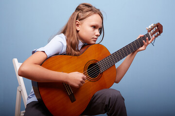 Fototapeta premium an 11-year-old girl is practicing a melody on a guitar on a blue background