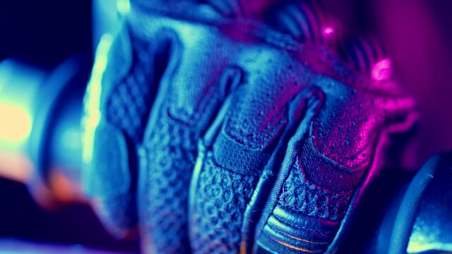 Close-up of bikers hand on road gloves who twists accelerometer lever while standing at traffic light in night city. Motorcycle, nightlife and driver culture concept.